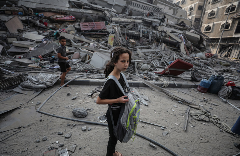 Child standing in front of a destroyed building